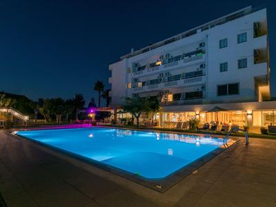 Ein beleuchteter Pool vor einem großen Hotelgebäude bei Nacht.