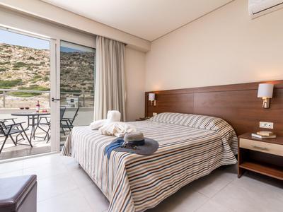 Gemütliches Hotelzimmer mit Doppelbett, Balkon und Blick auf eine felsige Landschaft.