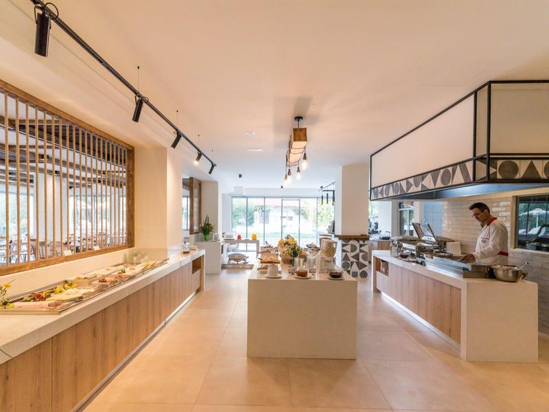 Moderner Frühstücksraum mit Buffet, hellem Holz, großen Fenstern und gedeckten Tischen.