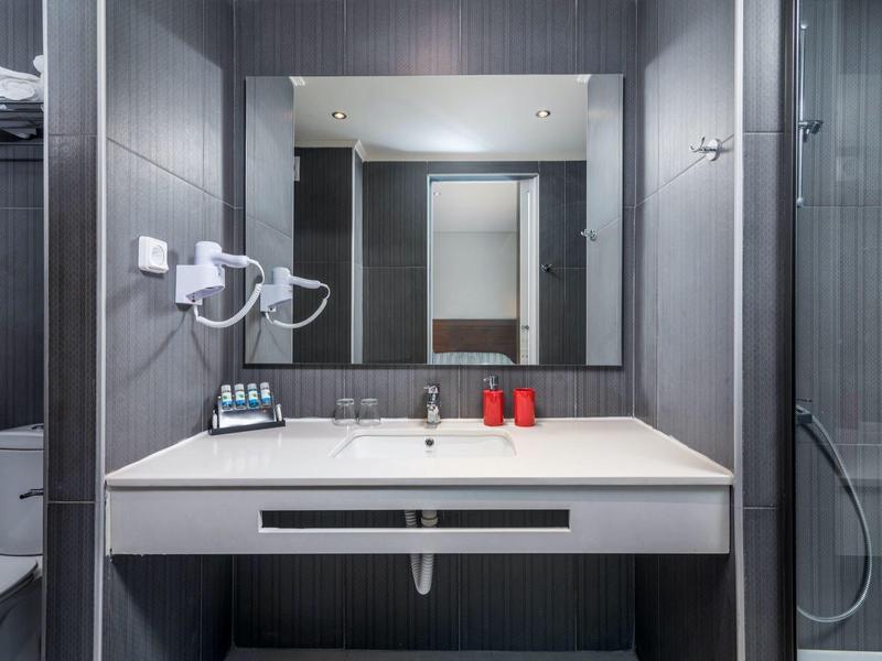 Moderner Badezimmerspiegel mit Waschbecken, Seifenspendern, Handtuchhaltern und dunklen Wandfliesen.