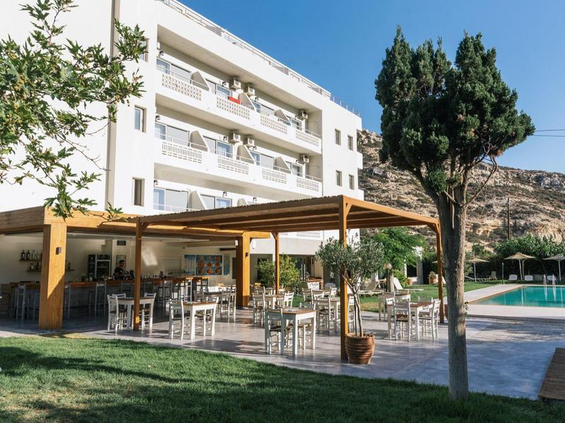 Moderner Hotelgarten mit Terrasse, Tischen, Stühlen, Pool, Bäumen und Bergen im Hintergrund.