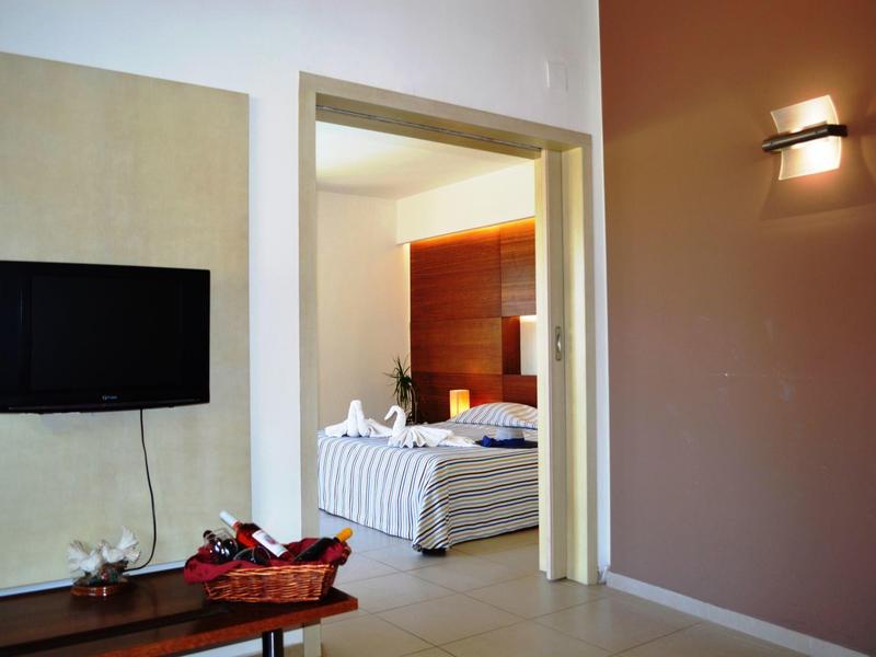 Moderner Raum mit Wand-TV, Holztisch, offener Tür zum Schlafzimmer mit Bett und warmem Licht.