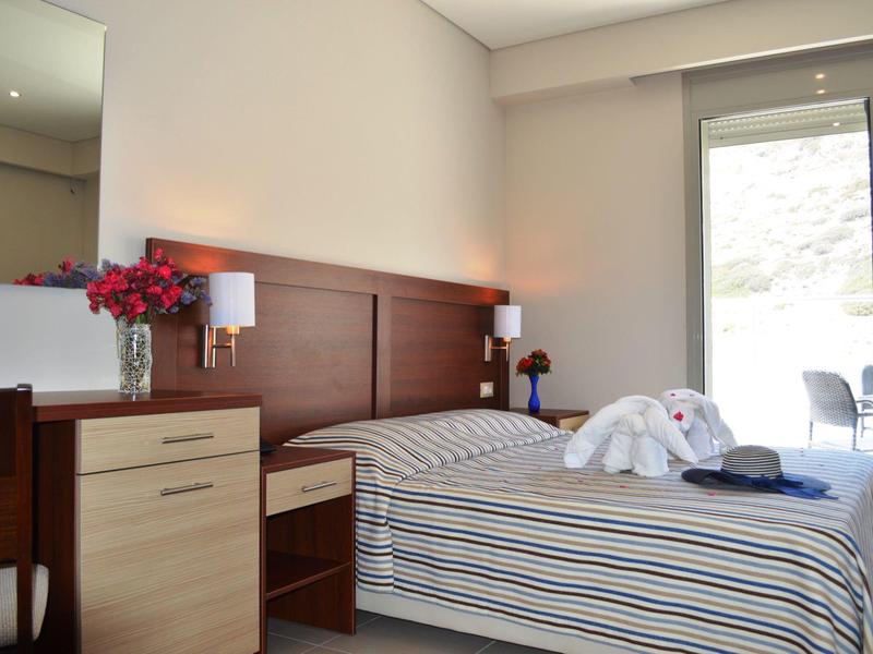 Helles Schlafzimmer mit Doppelbett, Holzmöbeln, Blumentopf und Terrassentür zu Balkon.