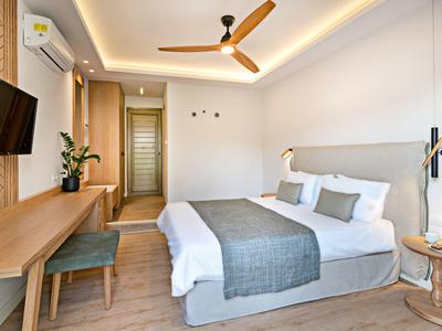 Habitación de hotel moderna con cama doble, escritorio, TV y ventilador de techo, iluminada y minimalista.