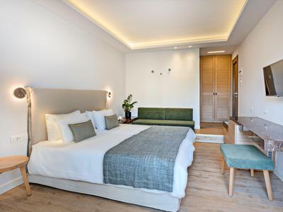 Habitación de hotel luminosa con cama doble grande, lámparas modernas y mobiliario sencillo en tonos neutros.