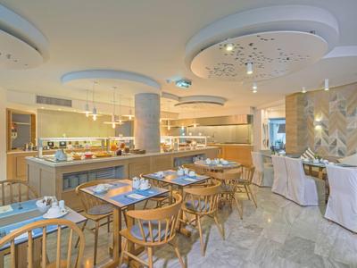 Área luminosa de restaurante de hotel con mesas de madera, sillas y modernas luces de techo.