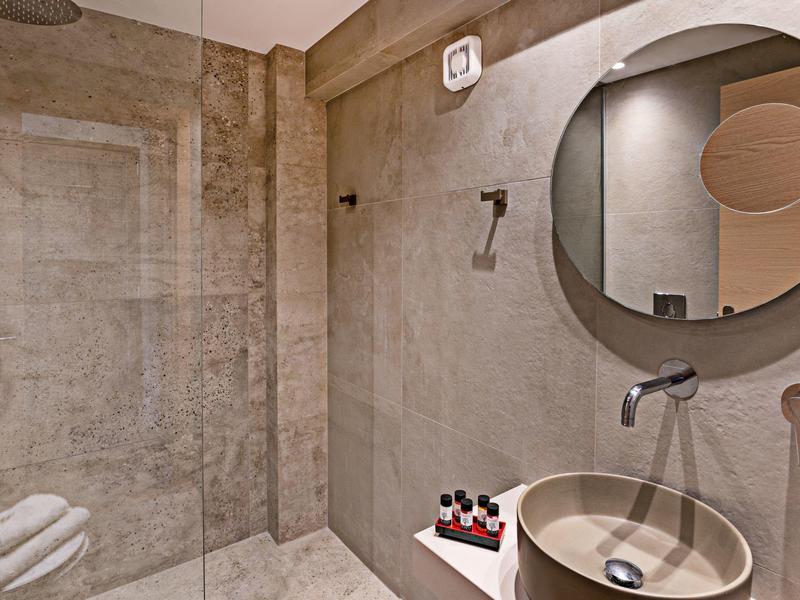 Baño moderno con espejo redondo, lavabo y toallas en tonos neutros.