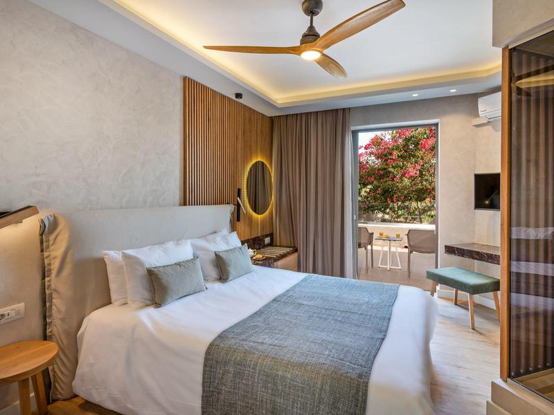 Habitación de hotel moderna con cama doble, materiales de madera y vista a terraza con flores.