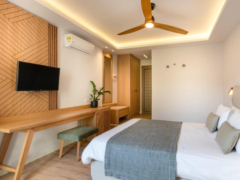 Habitación de hotel moderna con detalles de madera, cama doble, escritorio, televisor y ventilador de techo.