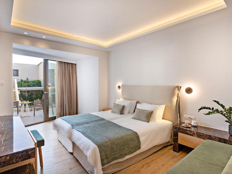 Habitación de hotel moderna con cama grande, balcón y luz indirecta cálida en el techo.