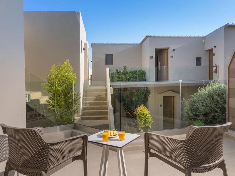 Patio moderno de hotel con dos sillas y una mesa con jugo de naranja bajo luz natural.