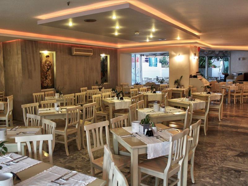 Restaurante de hotel luminoso y acogedor con mesas de madera y sillas blancas, decorado con flores.