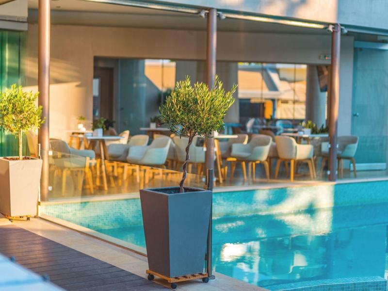 Área moderna de piscina de hotel con asientos y plantas bajo el sol.