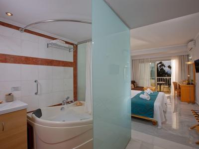 Nowoczesny pokój hotelowy z wanną, łóżkiem z niebieskim kocem i balkonem z widokiem na zewnątrz.