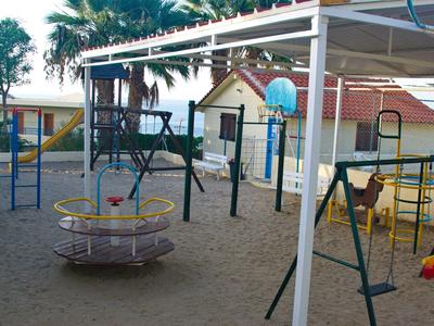 Plac zabaw dla dzieci z karuzelą, huśtawkami i piaskowym podłożem pod daszkiem.