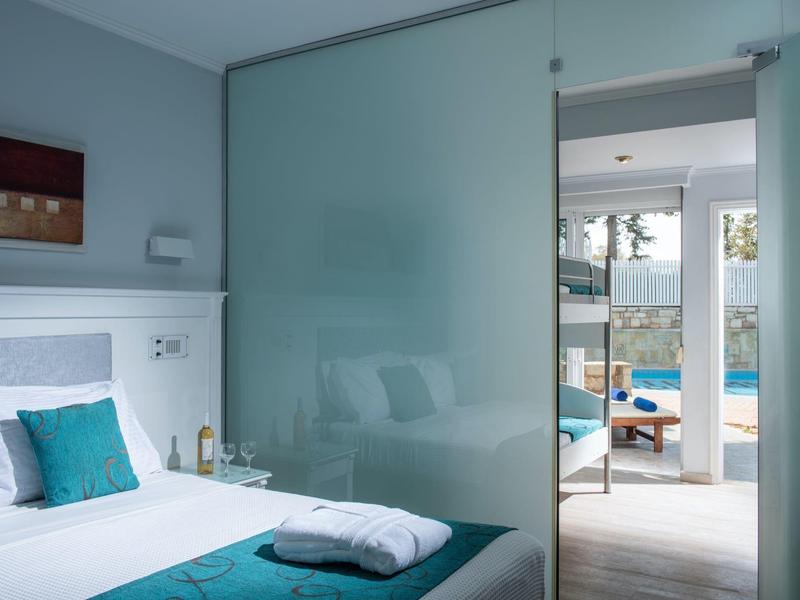 Nowoczesny obszar pokoju hotelowego z otwartym widokiem na basen i taras przez przesuwane drzwi ze szkła matowego.