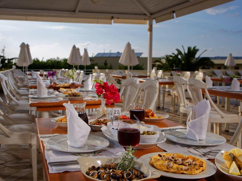 Restauracja na świeżym powietrzu nad morzem z nakrytymi stołami i widokiem na wybrzeże o zachodzie słońca.