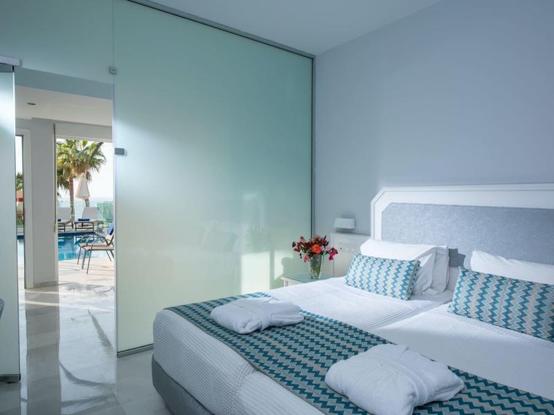 Jasny pokój hotelowy z łóżkiem podwójnym, pasiastą pościelą i widokiem na basen przez szklane przesuwne drzwi.