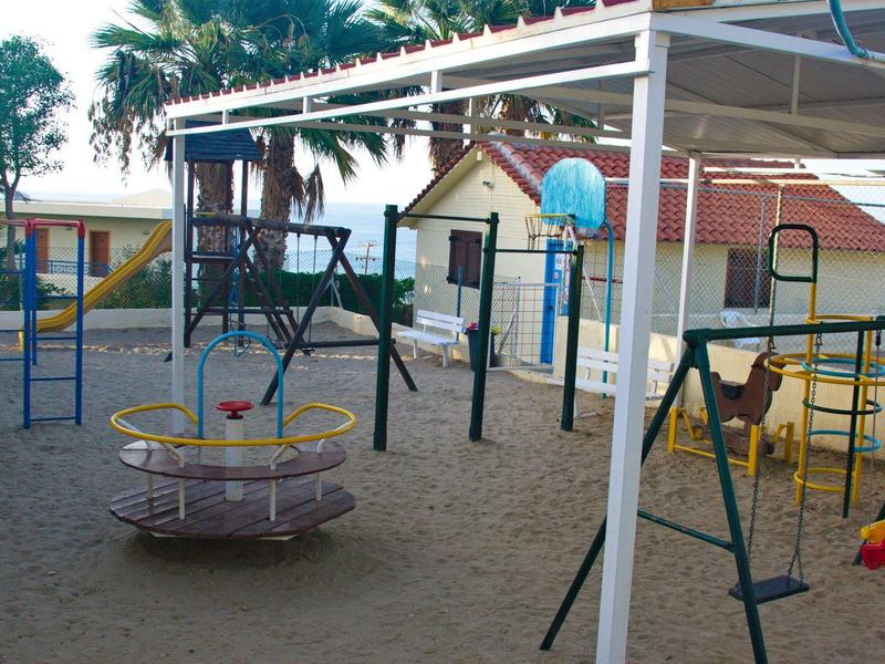 Plac zabaw dla dzieci z karuzelą, huśtawkami i piaskowym podłożem pod daszkiem.