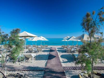 Strandpromenade mit Liegestühlen und Sonnenschirmen vor klarem blauem Meer und Himmel.