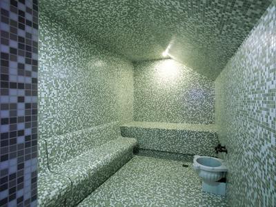 Łaźnia parowa z mozaikowymi kafelkami na ścianach, ławkach, podłodze oraz misą z wodą.