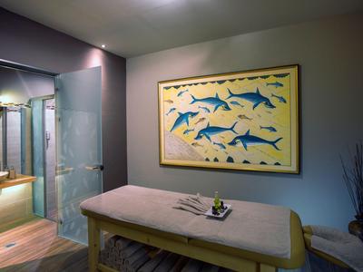 Spokojny pokój do masażu z stołem do masażu i obrazem niebieskich ryb na ścianie.