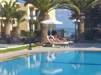 Schwimmbad mit blauer Wasserfläche, Palmen und Liegen mit Sonnenschirm in sonniger Anlage.