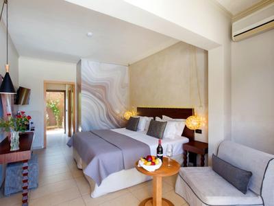 Modernes Hotelzimmer mit Doppelbett, Sitzbereich, Tisch mit Obst und Wein sowie Klimaanlage.