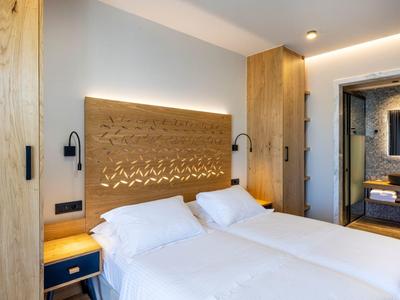 Modernes Hotelzimmer mit zwei Einzelbetten, Holzakzenten und indirekter Beleuchtung.