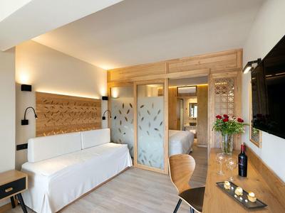 Modern eingerichtetes Hotelzimmer mit Couch, Holzmöbeln und einem großen TV an der Wand.