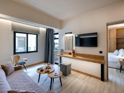 Modern eingerichtetes Hotelzimmer mit Sofa, Flachbildschirm und Blick auf ein angrenzendes Schlafzimmer.