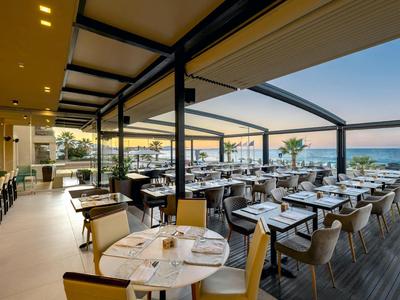 Nowoczesna przestrzeń gastronomiczna z miejscami do siedzenia i widokiem na morze o zachodzie słońca.