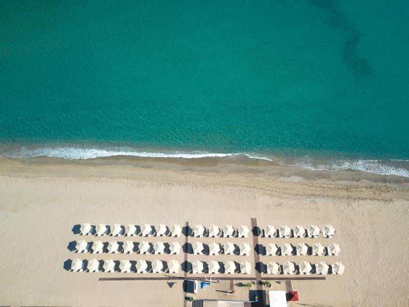 Luftaufnahme eines ruhigen Strandes mit Reihen von Sonnenschirmen und Liegestühlen am Sandstrand.