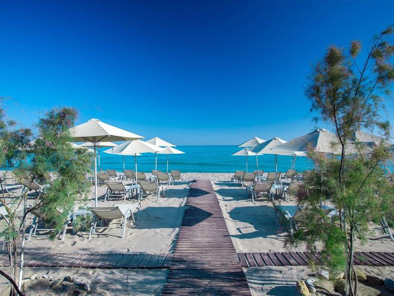Strandpromenade mit Liegestühlen und Sonnenschirmen vor klarem blauem Meer und Himmel.