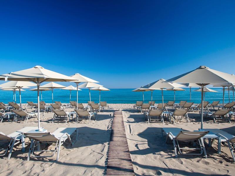 Strand mit Sonnenschirmen, Liegestühlen und Holzsteg zum Meer an einem klaren Tag