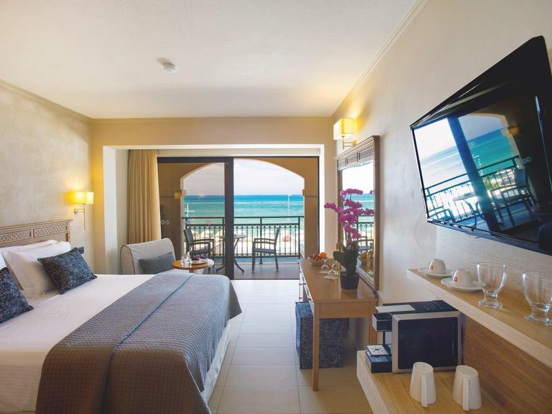 Modernes Hotelzimmer mit Bett, Fernseher und Zugang zu einem Balkon mit Meerblick.