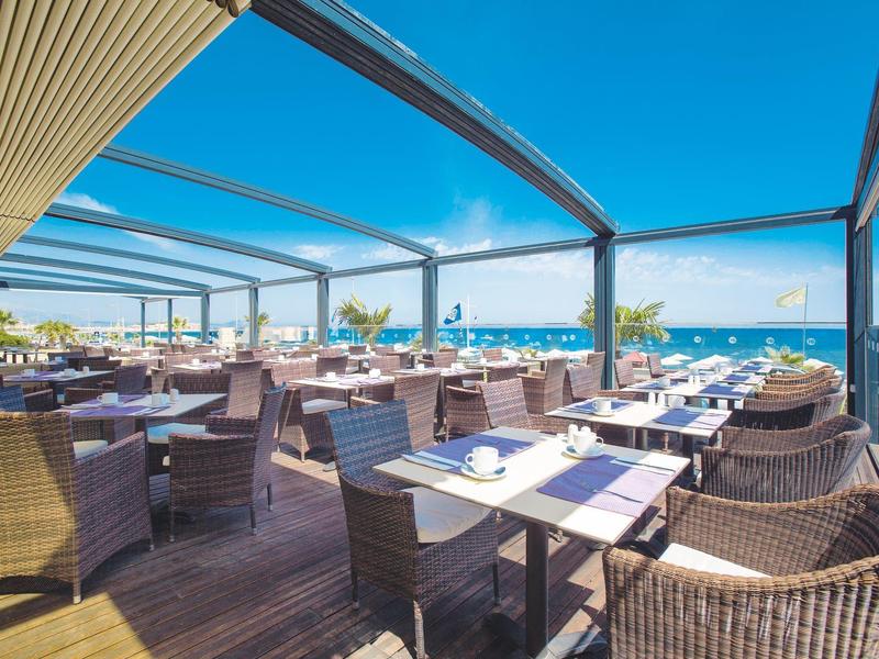 Offene Terrasse mit Korbstühlen und Tischen, Blick auf das Meer unter klarem Himmel.