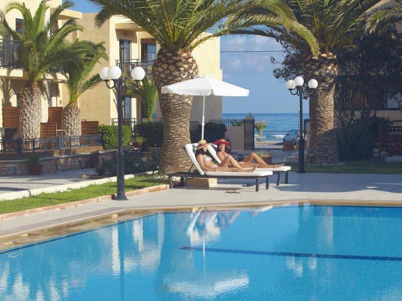 Schwimmbad mit blauer Wasserfläche, Palmen und Liegen mit Sonnenschirm in sonniger Anlage.