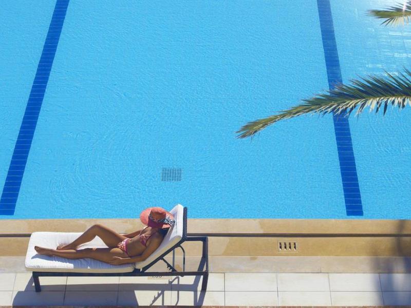 Eine entspannte Person liegt auf einer Liege neben einem blauen Schwimmbecken mit schwarzen Bahnlinien.