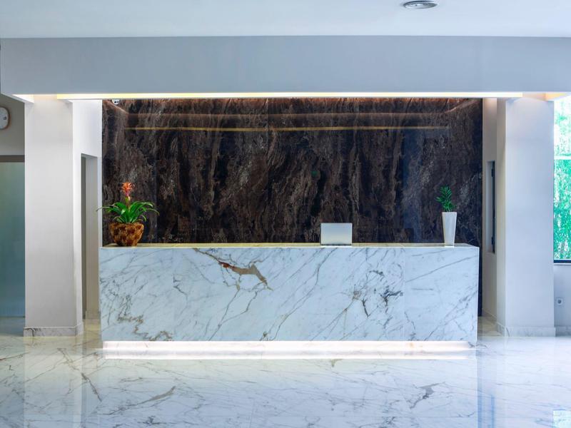 Moderner Hotel-Check-in mit weißem Marmortresen und dunkler Wand, frische Blumen als Dekor.