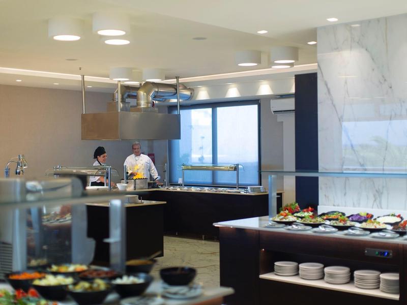 Moderne Hotelküche mit Köchen beim Zubereiten von Speisen und Buffet im Vordergrund.