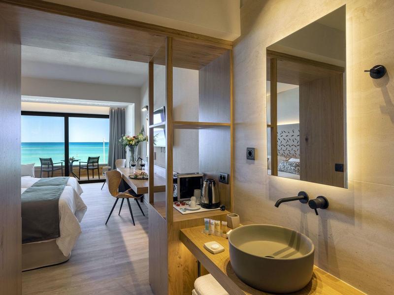 Modernes Hotelzimmer mit Blick auf das Meer, helles Bad mit Rundwaschbecken und Holzdetails