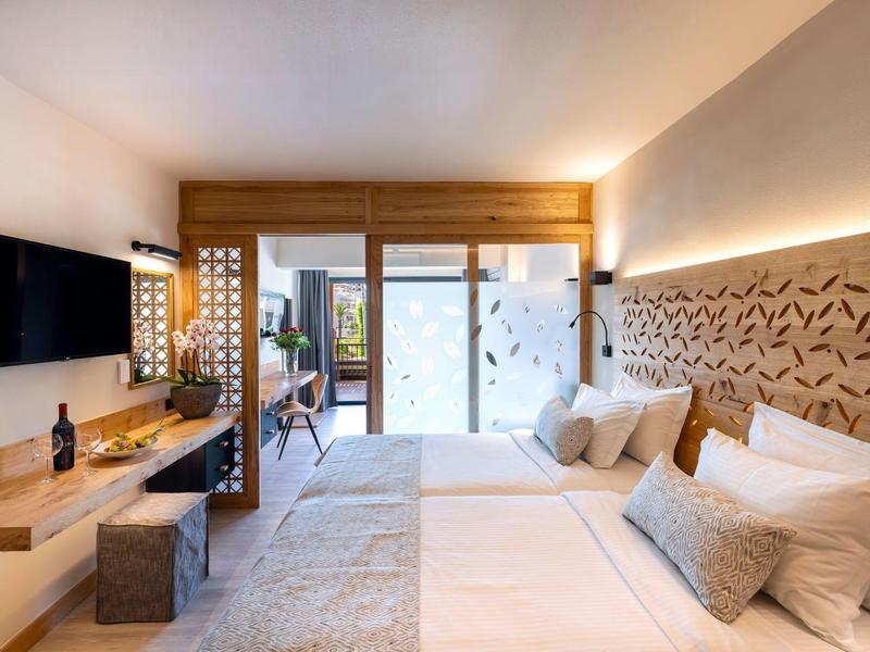 Modernes Hotelzimmer mit zwei Betten, TV, Schreibtisch und Terrasse mit Stühlen.