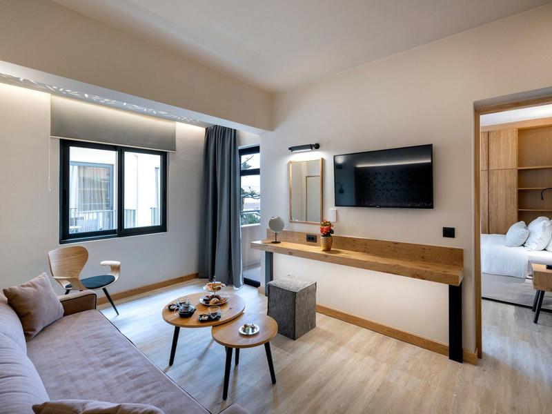 Modern eingerichtetes Hotelzimmer mit Sofa, Flachbildschirm und Blick auf ein angrenzendes Schlafzimmer.