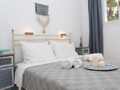 Camera luminosa con letto bianco, copriletto grigio, candele e asciugamani sul letto.