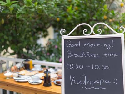 Pizarra negra con horario de desayuno junto a una mesa de madera al aire libre preparada.