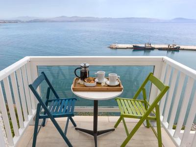 Balcone con sedie blu e verdi e servizio da caffè con vista sul mare.
