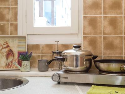 Cucina moderna con fornello, pentole, padella e piastrelle decorative sotto una finestra.