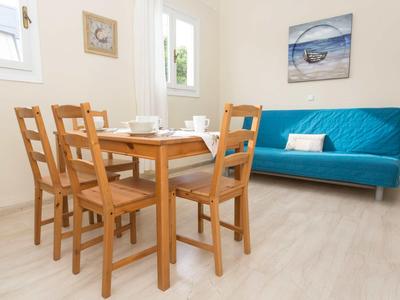 Zona pranzo luminosa con tavolo in legno, quattro sedie e divano blu contro parete bianca.