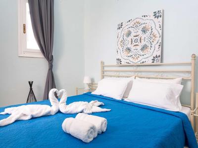 Letto matrimoniale con copriletto blu, cuscini bianchi e asciugamani a forma di cigno in una stanza luminosa.